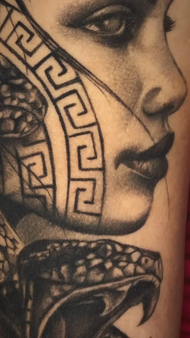 Dettaglio di un tatuaggio realistico: volto femminile con greca e serpente