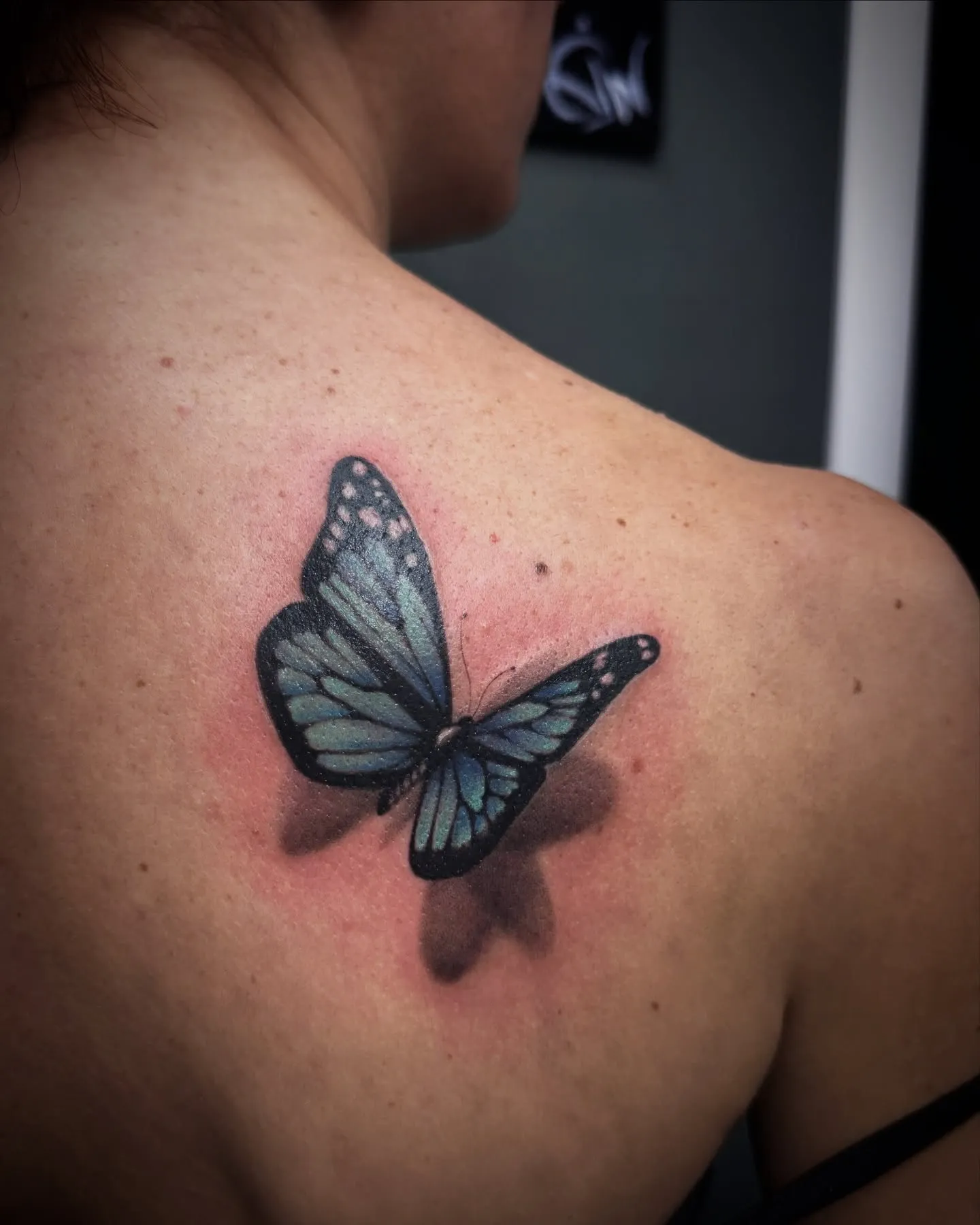 Tatuaggio a colori di una farfalla con effetto tridimensionale sulla scapola
